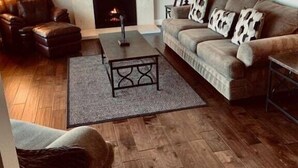 A cozy living room with a fireplace, leather sofas, a coffee table, and a patterned rug.