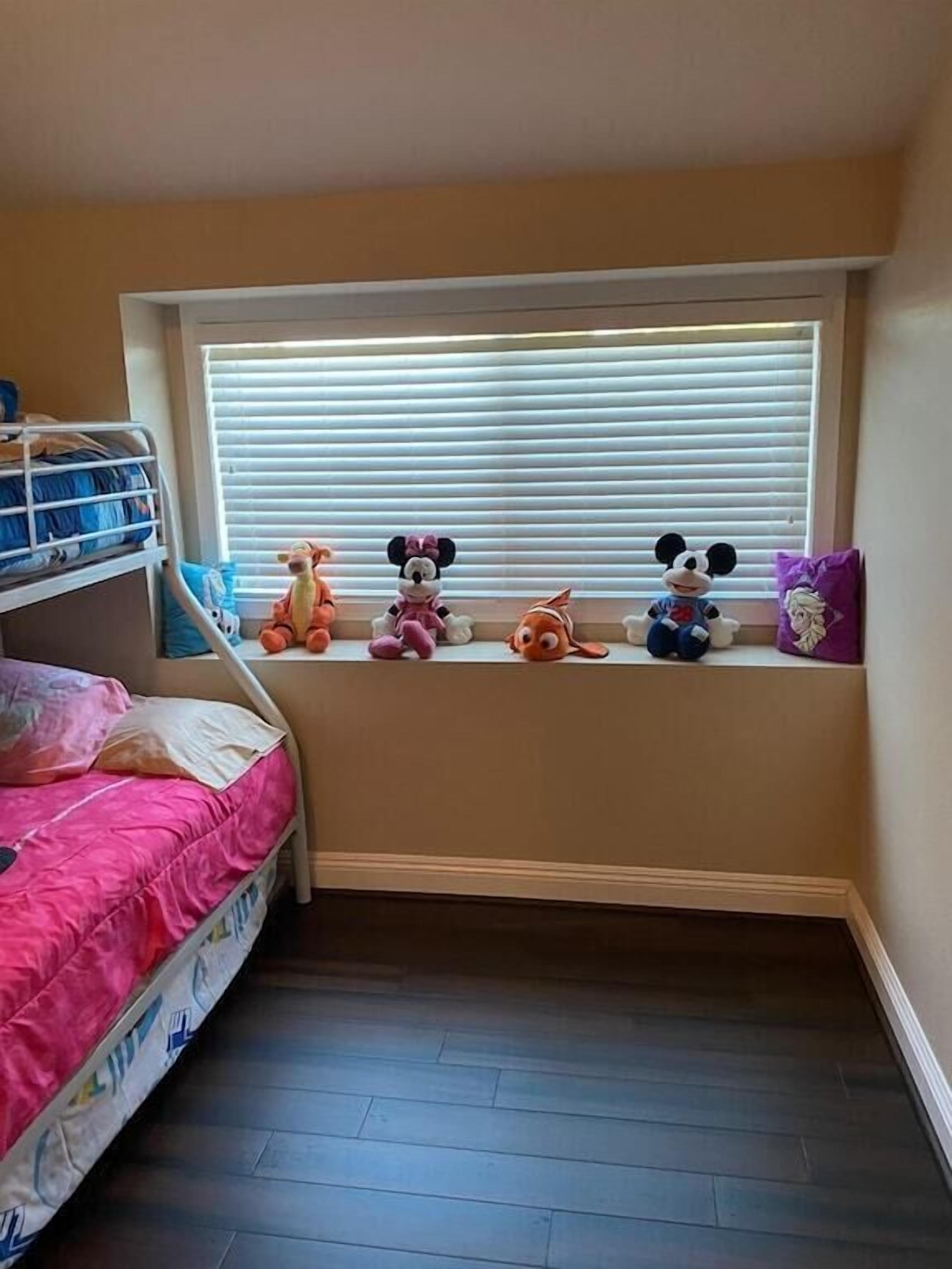 Habitación infantil con literas, una ventana con persianas y peluches en el alféizar.