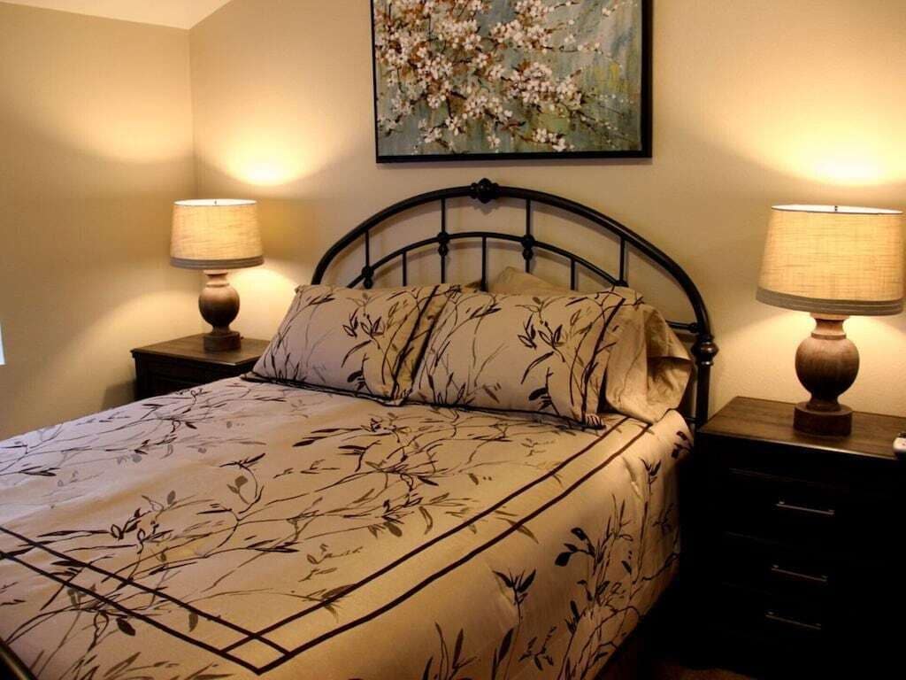 Un dormitorio con una cama, dos mesitas de noche con lámparas y un cuadro floral en la pared.