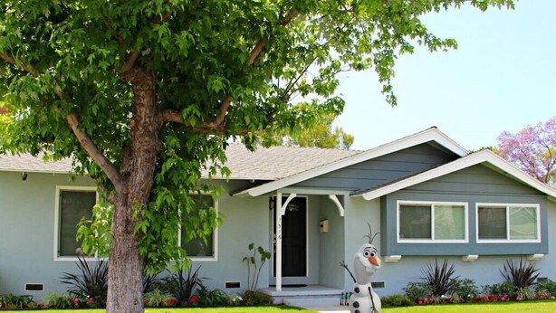 A house with a front porch, a tree, and a garden with flowers.