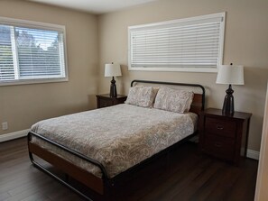 A bedroom with a bed, two nightstands, two lamps, a window with blinds, and a door.