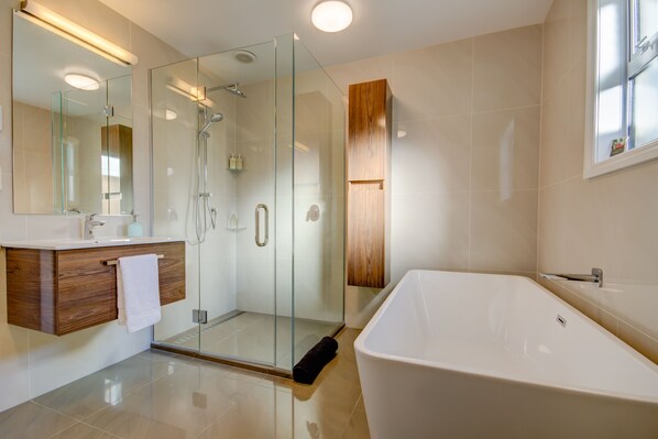A modern bathroom with a glass-enclosed shower, a wooden vanity, and a freestanding bathtub.