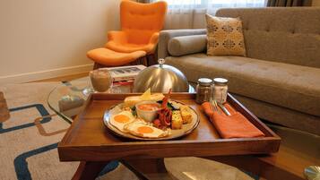 Ein Esstisch mit Frühstücksgebäck, ein Glastisch, eine Couch und ein orangefarbener Sessel in einem Wohnzimmer.