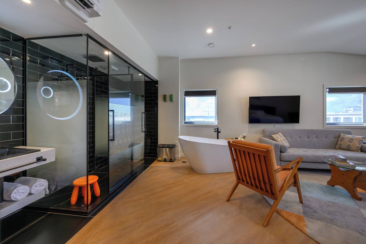 A modern bathroom with a glass shower enclosure, a freestanding bathtub, and a wooden stool.
