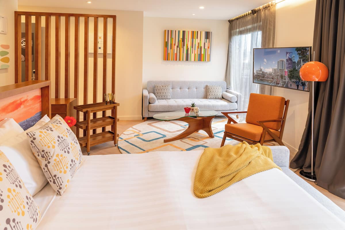A hotel room with a large bed, a sofa, a wooden side table, a coffee table, and a chair.