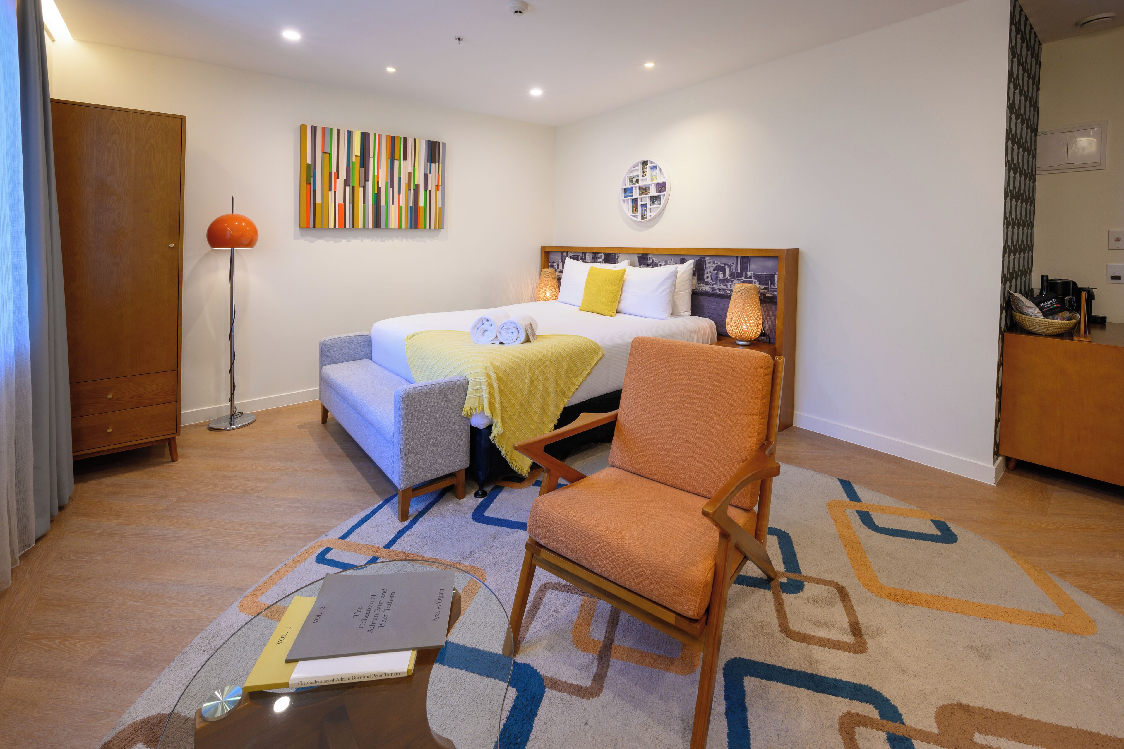 A hotel room with a bed, a chair, a desk, and a floor lamp.
