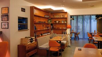 Ein gemütliches Hotelzimmer mit einer Holzbücherwand, einer Couch, einem Essbereich mit orangefarbenen Stühlen und einem großen Fenster mit Vorhängen.