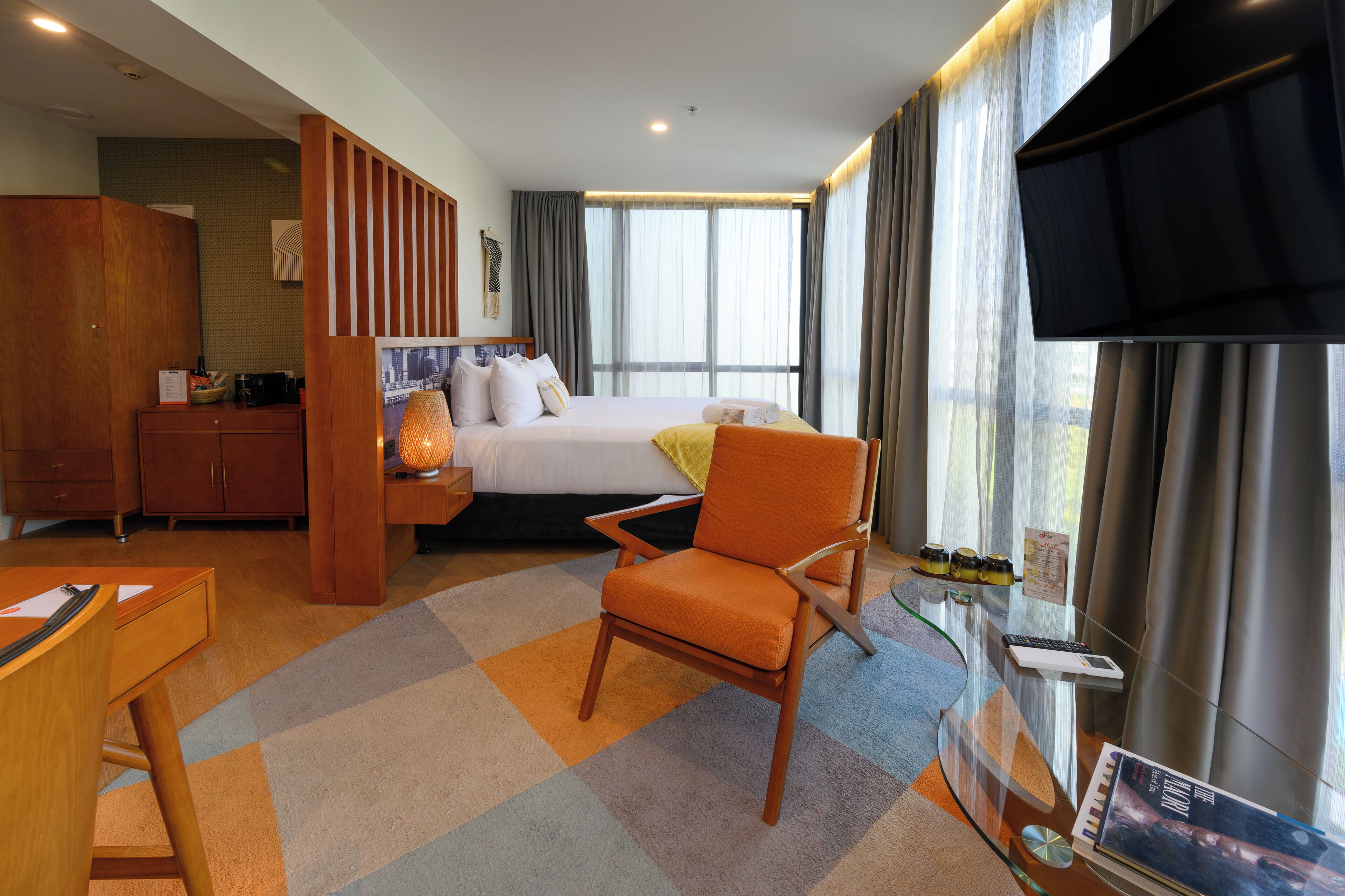 A hotel room with a bed, a desk, a chair, a TV, and a window with curtains.