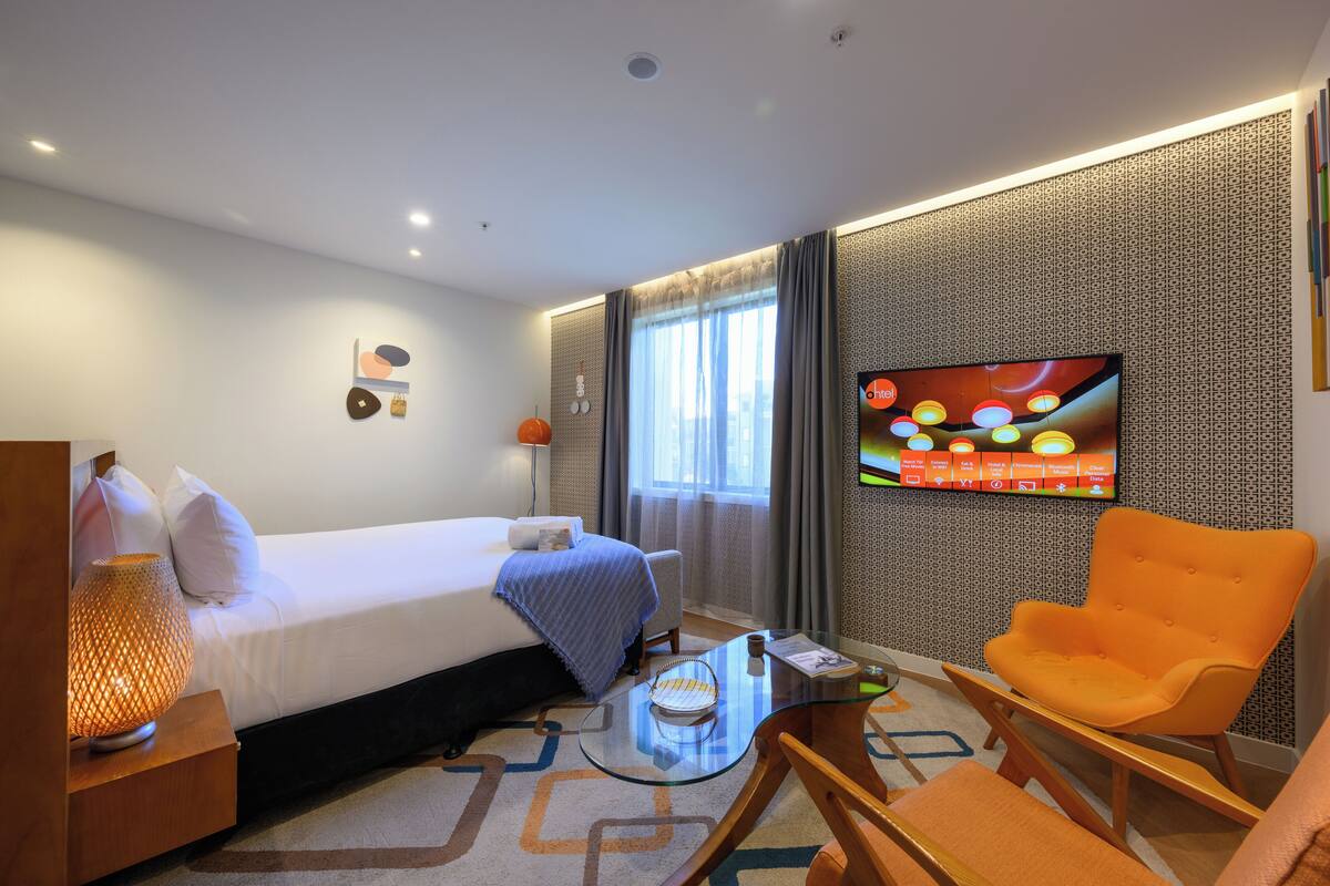 A hotel room with a bed, a TV, a chair, and a small table.