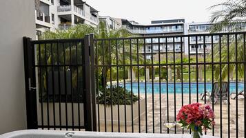 A hot tub with a view of a swimming pool and a tower in the background.