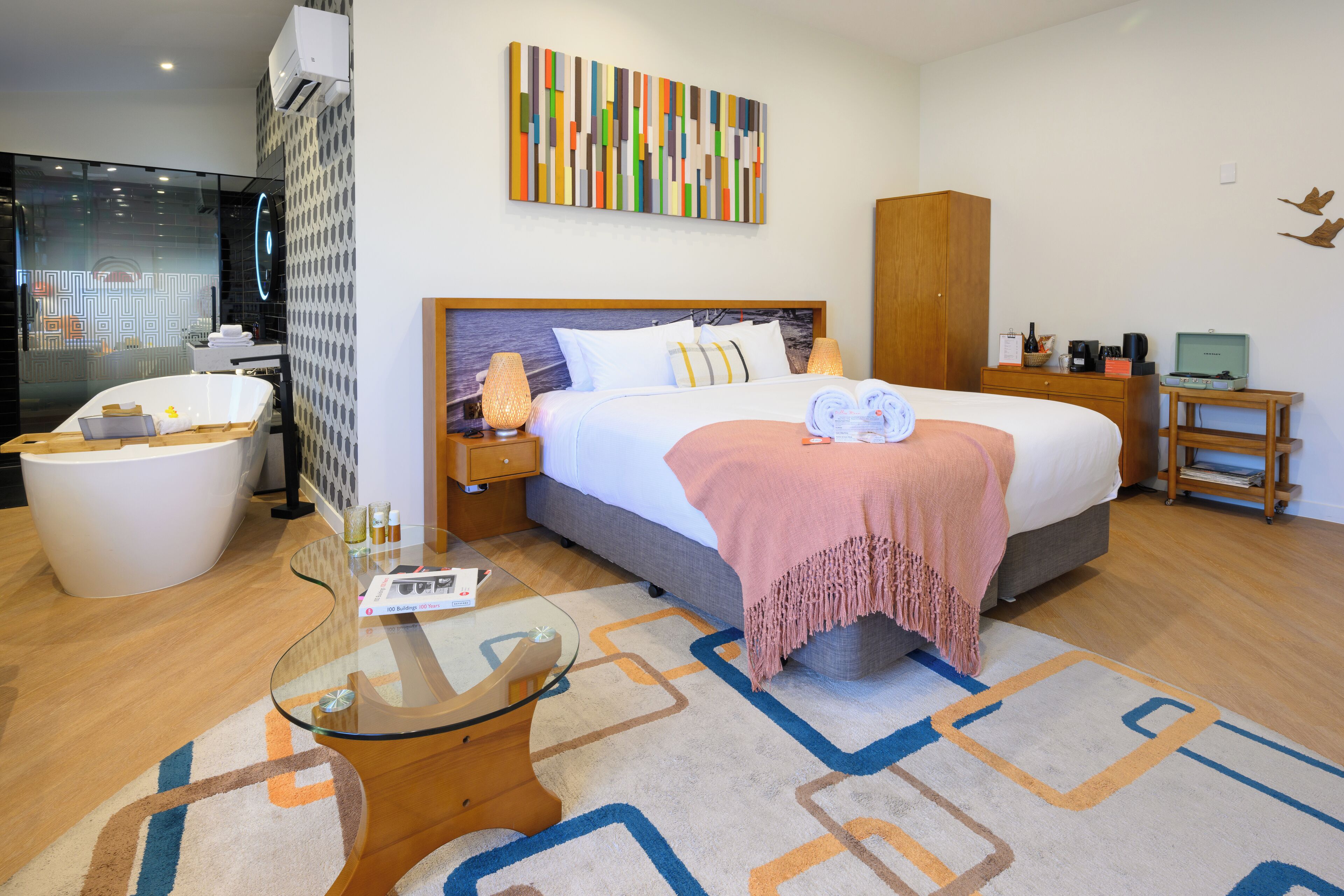 A modern hotel room with a large bed, a glass coffee table, a bathtub, and a wooden cabinet.
