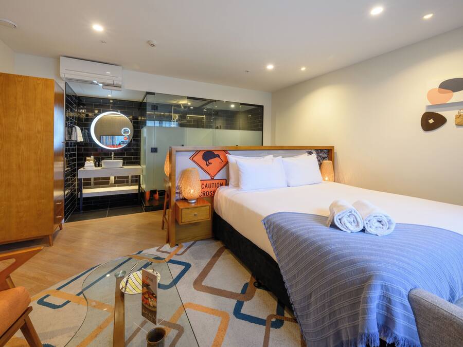 Een moderne hotelkamer met een groot bed, een nachtkastje met een lamp, een spiegel en uitzicht op de badkamer.