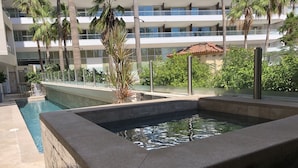 Ein Pool mit Steinrand, umgeben von Palmen und einem mehrstöckigen Gebäude mit Balkonen.