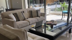 Ein modernes Wohnzimmer mit einem beigefarbenen Sofa, einem Glastisch und einem Laptop.