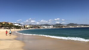 Ein Strand mit blauem Himmel, sandigem Ufer und Gebäuden im Hintergrund.