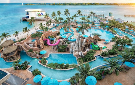 A resort with multiple swimming pools, palm trees, and a beach area.