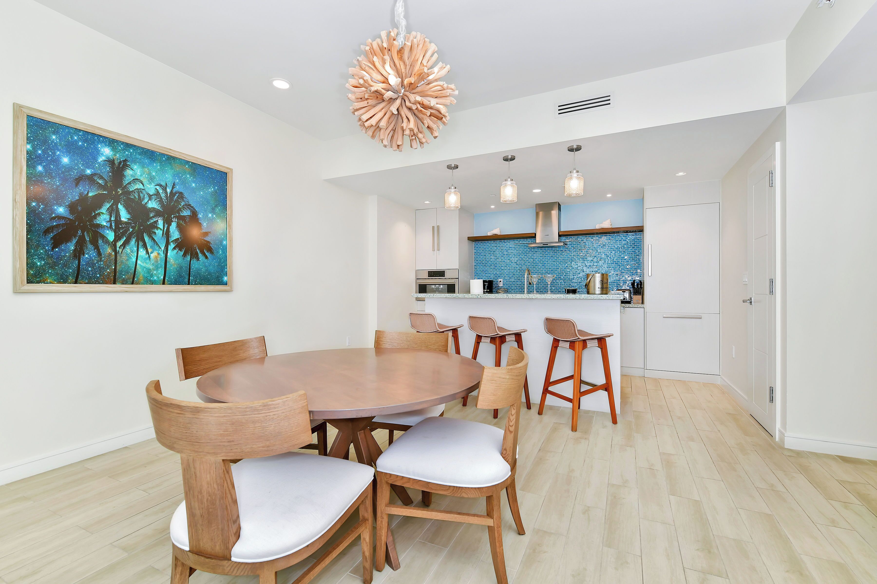 A modern kitchen with a blue backsplash, a dining area with wooden chairs and a round table, and a ceiling light fixture.