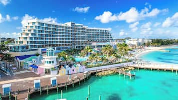 A large hotel with multiple floors, a beach, and a pier extending into turquoise waters.