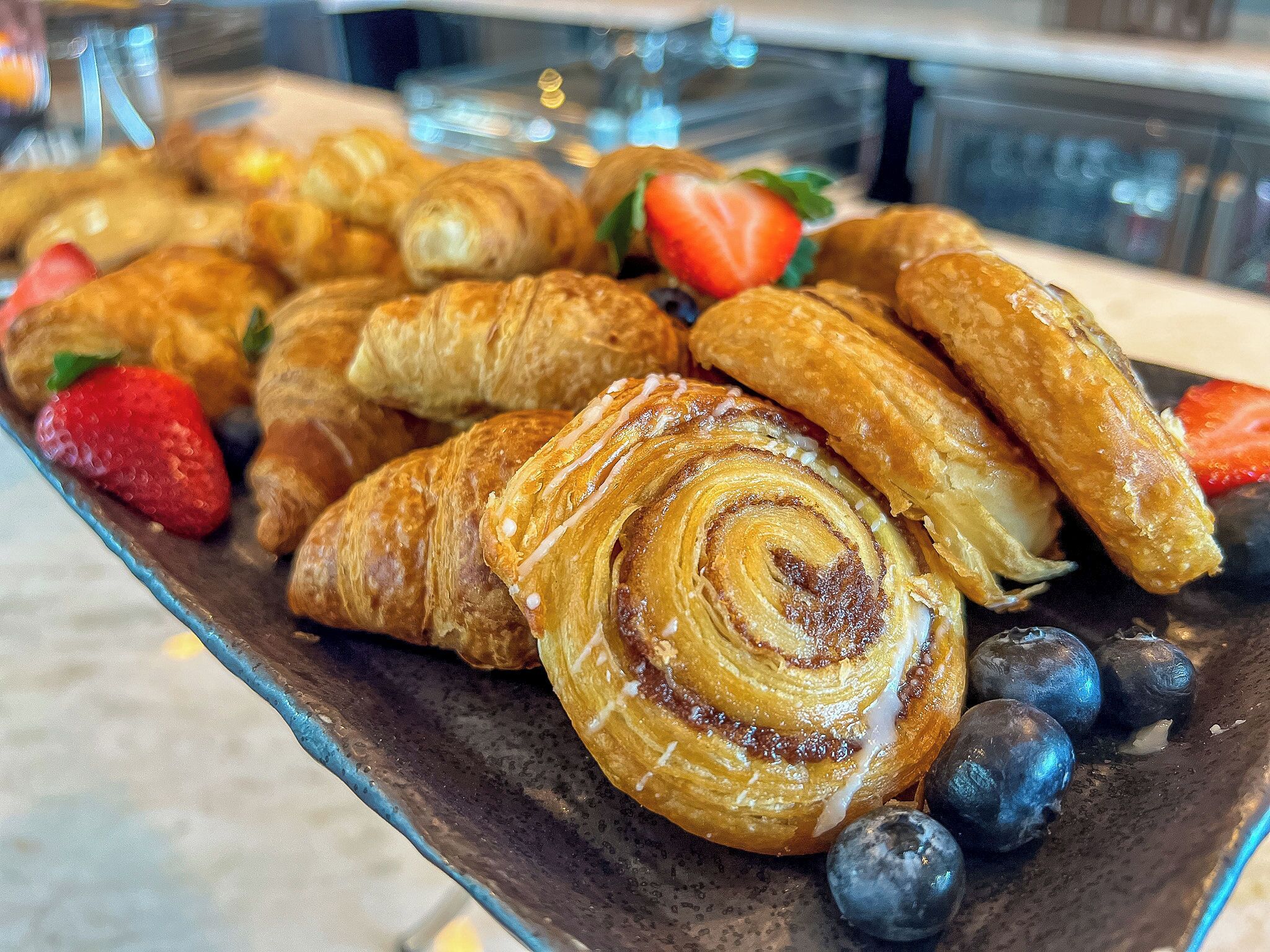 Una variedad de pasteles, incluyendo croissants y un pastel en espiral, acompañados de fresas y arándanos.