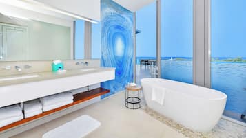 Een moderne badkamer met een groot bad, een wastafel met spiegel en uitzicht op de zee door grote ramen.