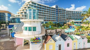 Un hotel grande con múltiples balcones, una zona de piscina y un cartel de resort en la playa.
