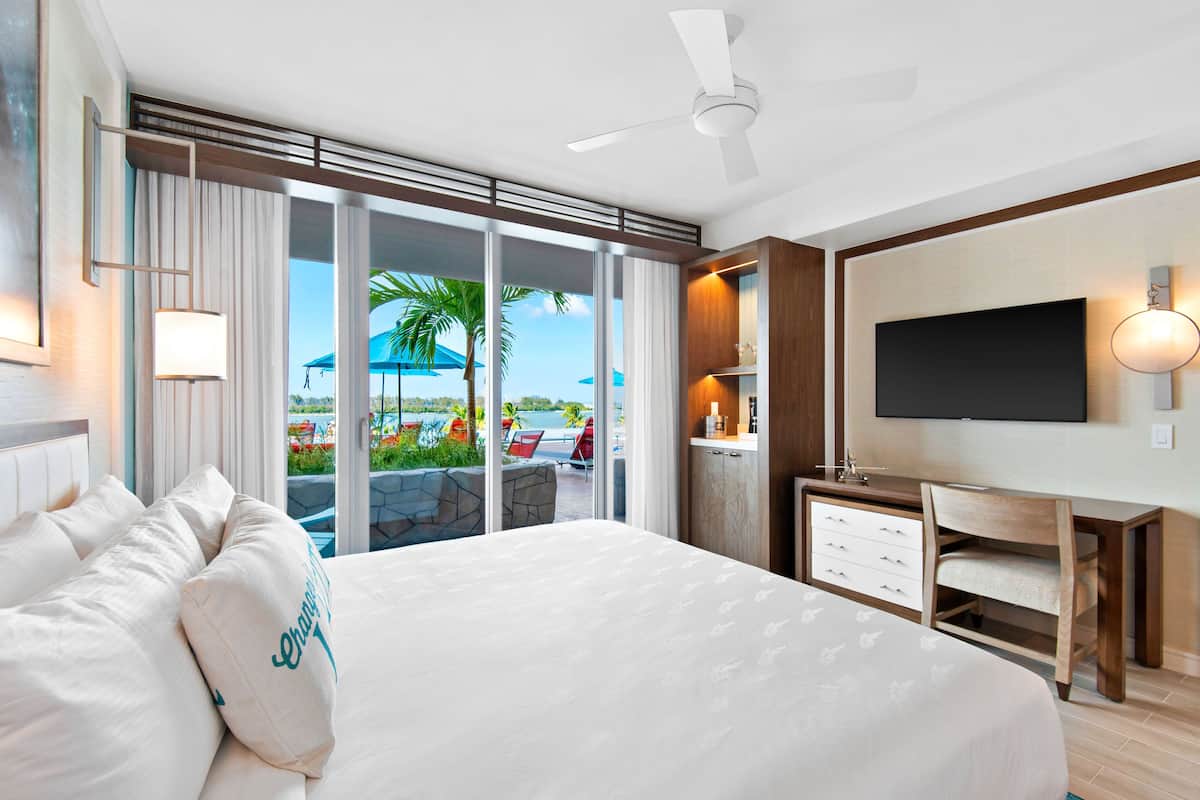 Ein Hotelzimmer mit einem großen Bett, einem Schreibtisch, einem Fernseher und Blick auf den Strand.