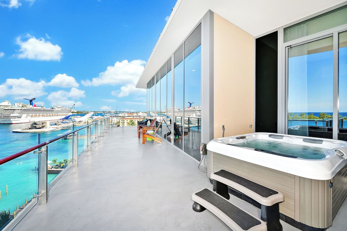 Ein Balkon mit Whirlpool, Glasgeländern und Blick auf das Meer, mit einem Kreuzfahrtschiff im Hintergrund.