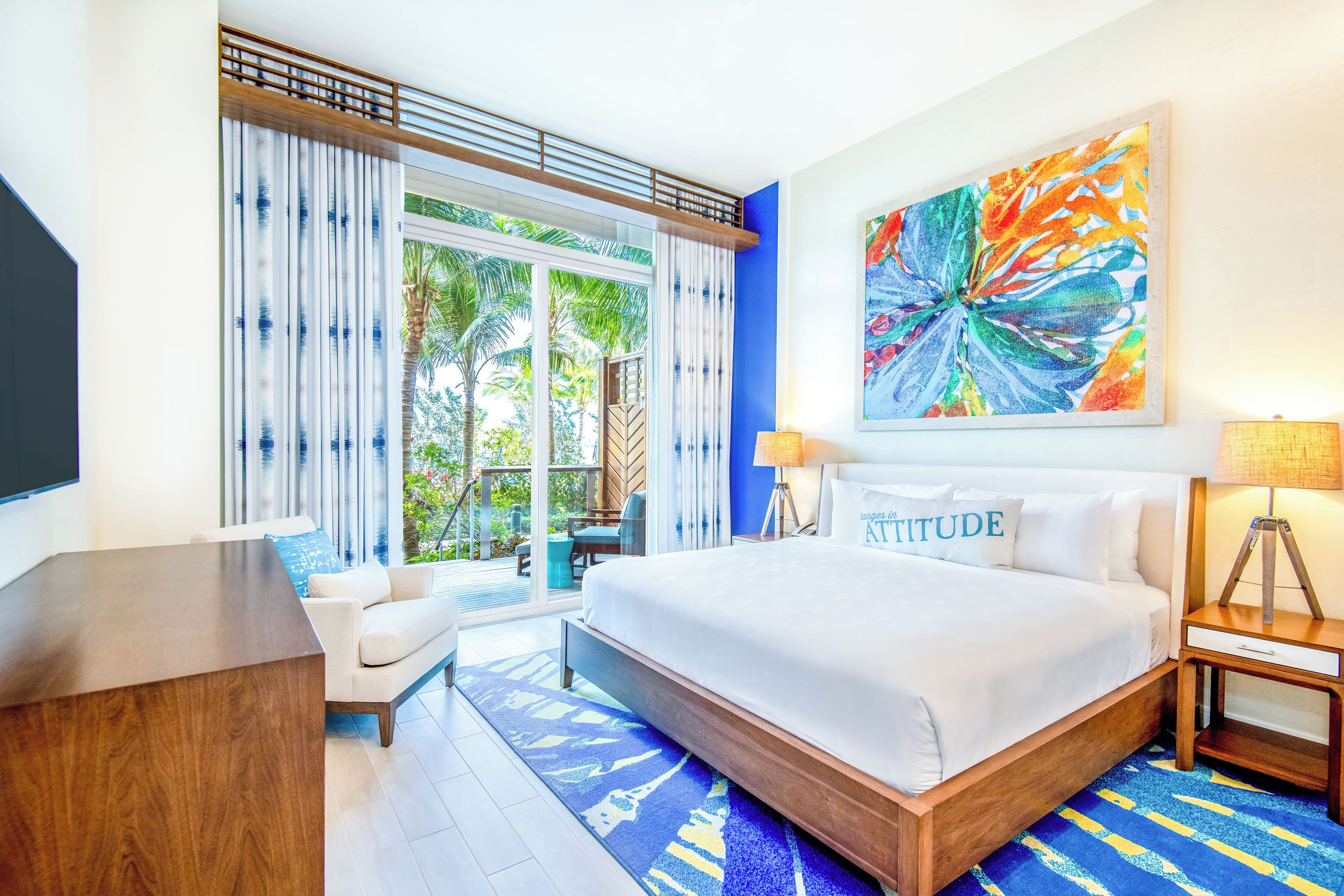 A hotel room with a large bed, a desk, a chair, a TV, and a window with curtains.