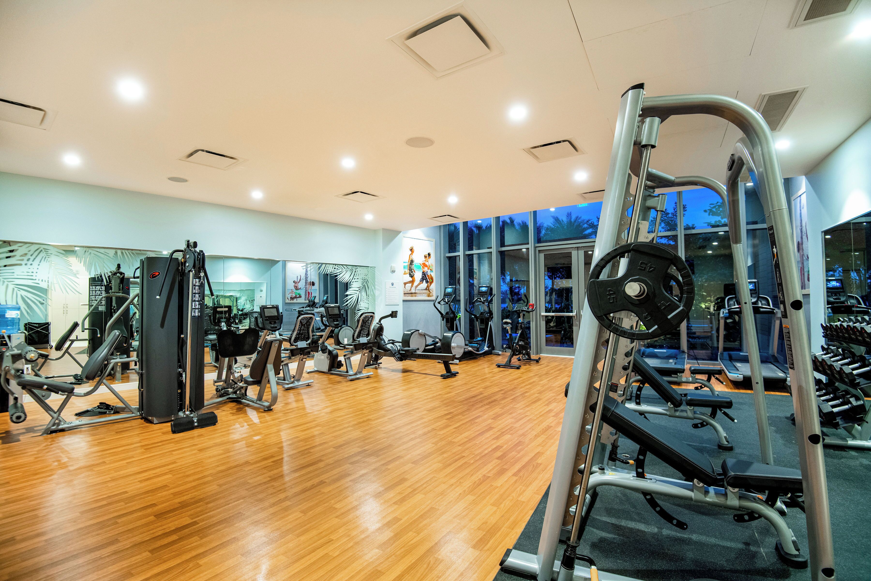 A gym with various exercise equipment, wooden flooring, and large windows.