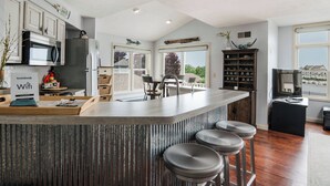 A modern kitchen with a central island, bar stools, a microwave, and a refrigerator. - Fully Updated Marina View Condo (Manistee)