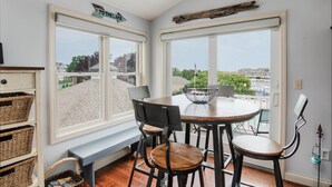 A dining area with a table and chairs, large windows, and a view of a residential area. - Fully Updated Marina View Condo (Manistee)