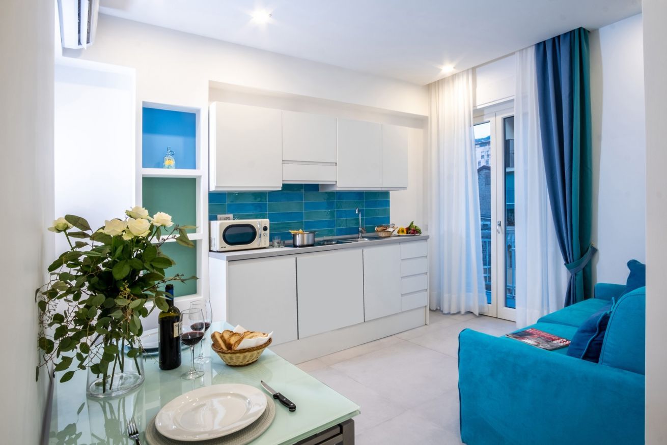 A modern kitchen with white cabinets, a blue backsplash, and a dining area with a table set for two.