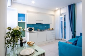 Een moderne keuken met witte kasten, een blauwe achterwand en een eethoek met een tafel voor twee personen.