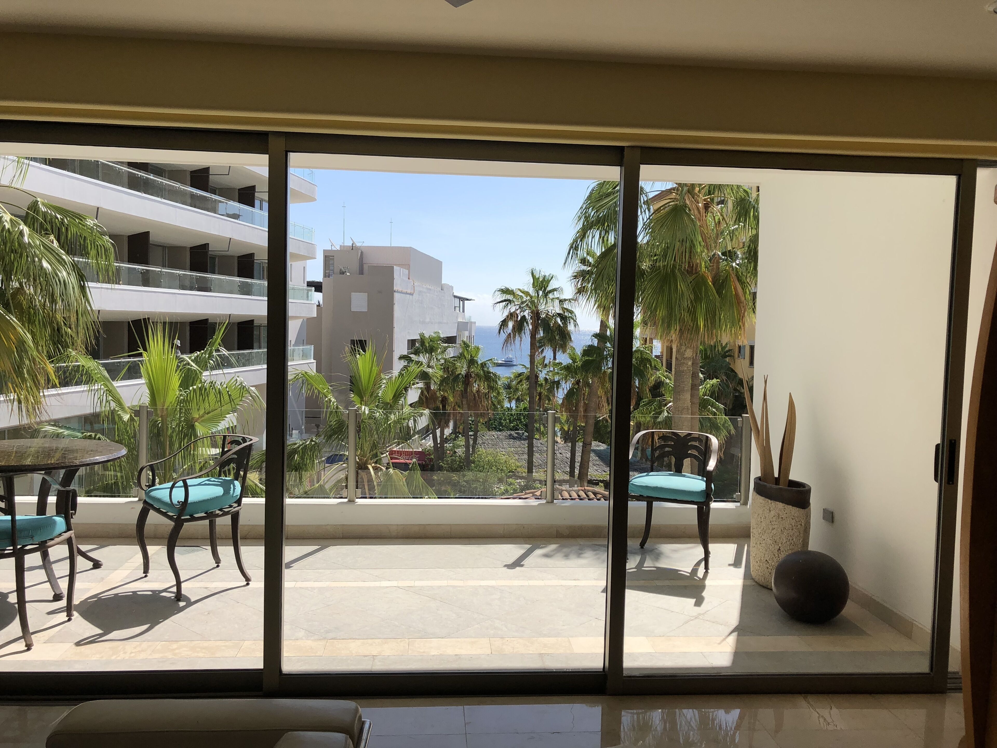 Un balcon avec vue sur un immeuble, des palmiers et une étendue d’eau.
