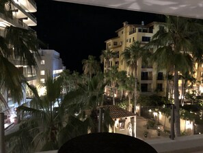 Een nachtzicht van een hotel met meerdere verdiepingen, palmbomen en een klein verlicht gebouw op de voorgrond.