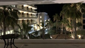 Een meerlaags hotel met balkons, palmbomen en uitzicht op een gebouw aan de overkant van de straat.