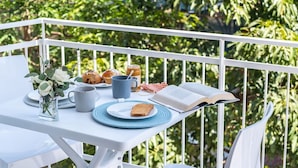 Un balcon avec une table blanche mise pour le petit-déjeuner, comprenant un livre, une tasse, des toasts et des viennoiseries.
