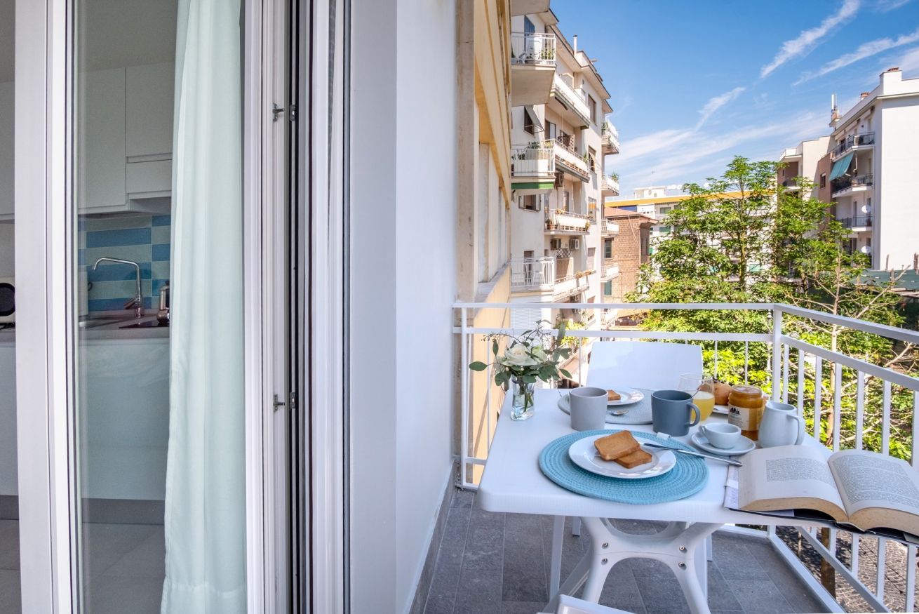 Un balcon avec une table préparée pour le petit-déjeuner, donnant sur un quartier résidentiel composé de plusieurs immeubles.