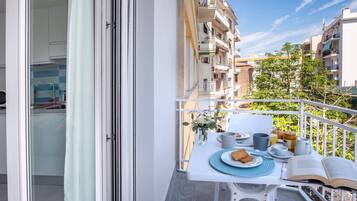 Un balcon avec une table préparée pour le petit-déjeuner, donnant sur un quartier résidentiel composé de plusieurs immeubles.