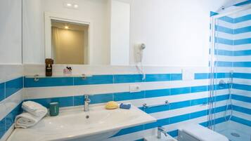 Une salle de bain avec un lavabo blanc, des carreaux à rayures bleues, un miroir, un sèche-cheveux et une douche.