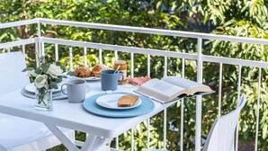 Un balcon avec une table préparée pour le petit-déjeuner, comprenant un livre, une tasse, des toasts et des viennoiseries.