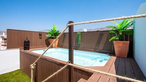 Une terrasse sur le toit avec un jacuzzi, entourée de rampes en bois et de plantes en pot.