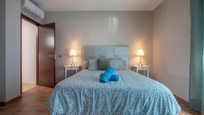 Une chambre à coucher comprenant un lit, deux tables de chevet, une tête de lit et un appareil de climatisation.