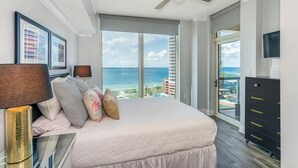 A bedroom with a large bed, a ceiling fan, a TV, and a view of the ocean. - P5-0905 2B Tower 5 @ Portofino! (Pensacola Beach)