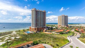 A high-rise hotel with a pool and a beach view, surrounded by palm trees and a clear sky. - P5-0905 2B Tower 5 @ Portofino! (Pensacola Beach)