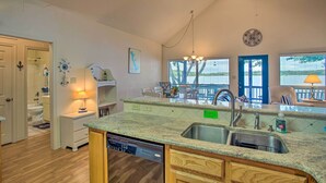 A kitchen with granite countertops, a dishwasher, and a sink. There is a dining area with chairs and a table, and a window with a view of the outdoors. - Private Dock & Fire Pit: Cedar Creek Lake Home (Eustace)
