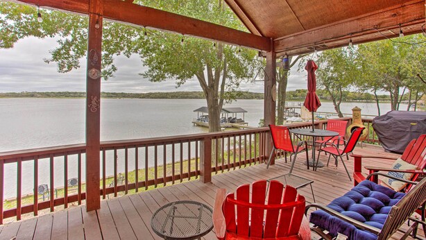 A covered deck with a view of a lake, red chairs, a table, and a grill. - Private Dock & Fire Pit: Cedar Creek Lake Home (Eustace)
