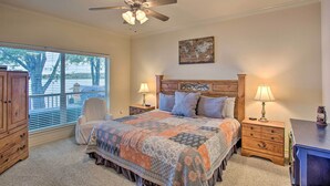 A bedroom with a large bed, two bedside tables with lamps, a ceiling fan, a wooden headboard, a window with blinds, and a view of trees outside. - Private Dock & Fire Pit: Cedar Creek Lake Home (Eustace)