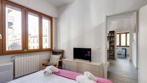 Un dormitorio con cama, televisión, silla, escritorio y estantería.