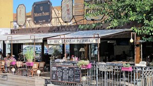 Un restaurant doté d’une terrasse, d’un tableau affichant le menu et d’une enseigne indiquant qu’il est ouvert en continu.